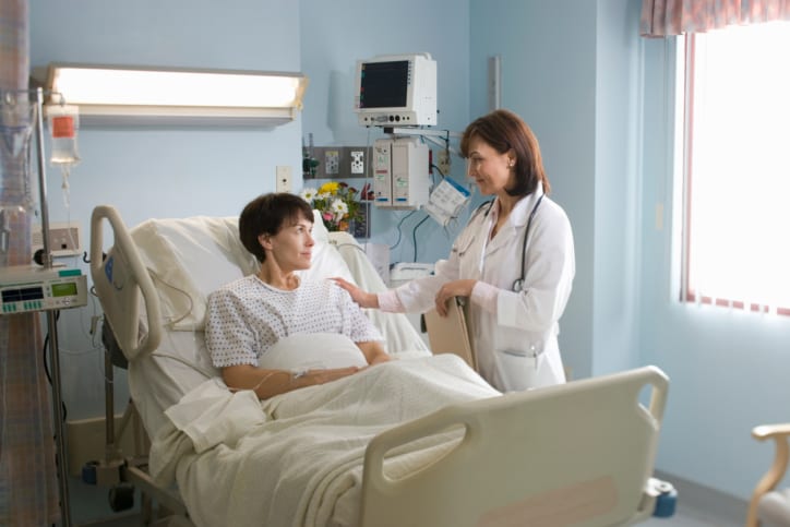 Female doctor comforting female patient lying in hospital bed