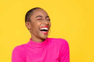 Happy optimistic African American woman in colorful pink clothes laughing isolated on yellow background. Results RNA anxiety relief