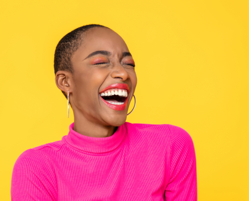 Happy optimistic African American woman in colorful pink clothes laughing isolated on yellow background. Results RNA anxiety relief