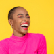 Happy optimistic African American woman in colorful pink clothes laughing isolated on yellow background. Results RNA anxiety relief